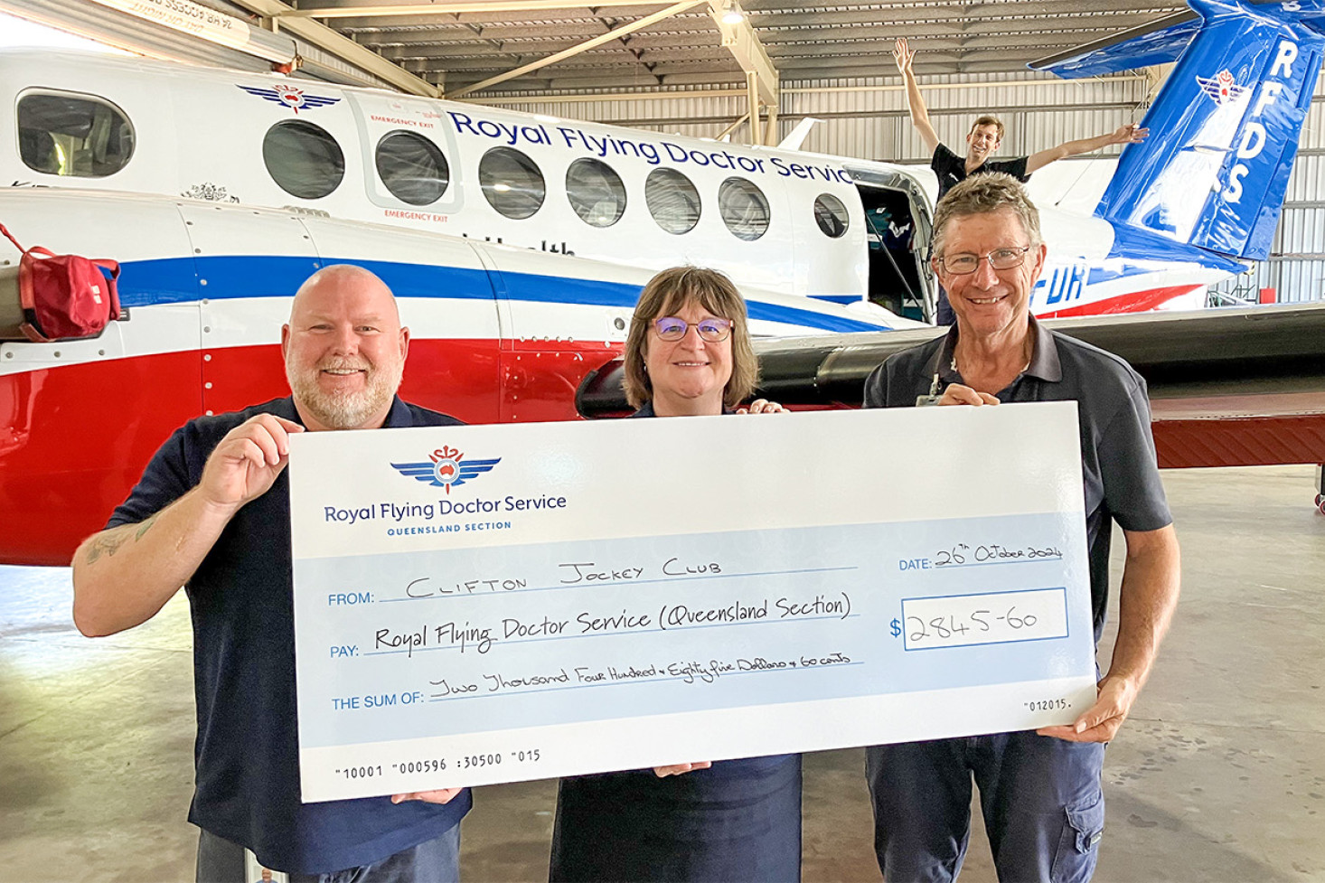 RFDS staff receive the cheque, from left, Justin and Gail (Base Support Managers), Bruce (Ground Support Officer) and an excited Cal (Engineer) in the background.