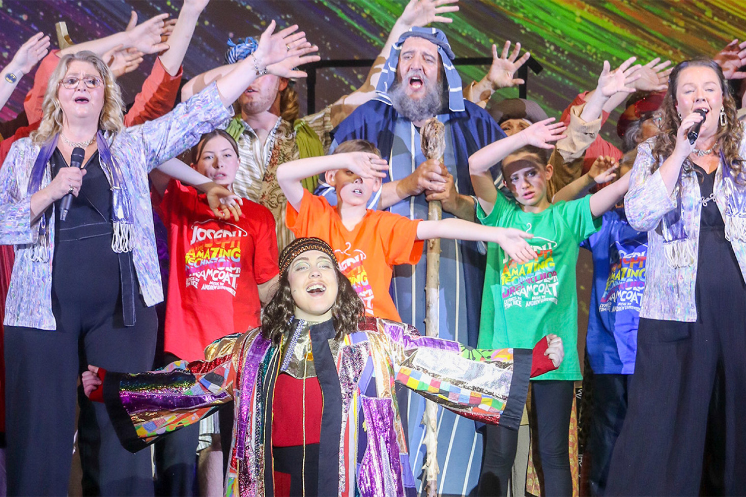 Phoebe Cheetham (Joseph) with Karen Rock (Narrator), Tony McEwan (Jacob), Nicole Sacagio (Narrator), and the youth choir on stage during the finale.
